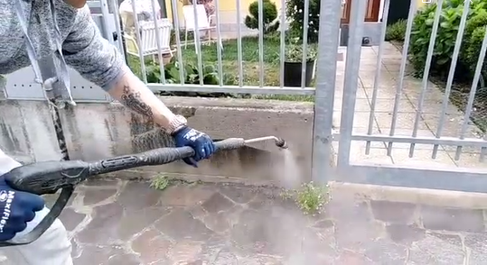 Immagine di una pulizia in corso ad un muretto, con la pisola idropulitrice